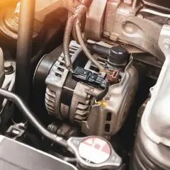 Zbliżenie na alternator samochodowy w komorze silnika, z widocznymi przewodami i złączami.
