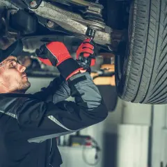 Mechanik w rękawiczkach dokręca sworzeń wahacza kluczem nasadowym pod podniesionym samochodem.