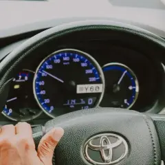 Ręce na kierownicy Toyoty, widoczne zegary i wskaźniki. Elektryczne wspomaganie kierownicy ułatwia jazdę.