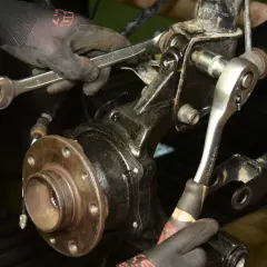 Mechanik w rękawiczkach dokonuje wymiany łożyska koła, używając kluczy do odkręcenia elementów zawieszenia.