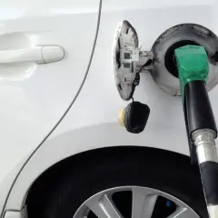 Tankowanie białego auta z użyciem bezkorkowego systemu wlewu paliwa. Zielona dysza dystrybutora w otworze wlewu.