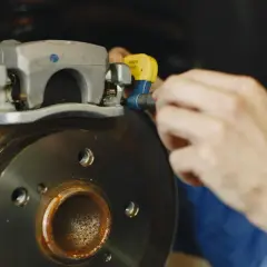 Mechanik sprawdza, czy klocek hamulcowy nie odbija od tarczy. Widoczny zacisk i skorodowana tarcza hamulcowa.