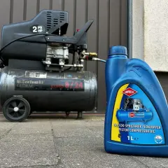Niebieska butelka z etykietą "OLEJ DO SPRĘŻAREK TŁOKOWYCH PISTON COMPRESSOR OIL" obok sprężarki Einhell.