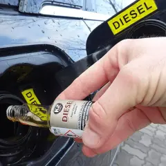 Dłoń wlewa dodatek do benzyny z małej buteleczki do baku diesla.