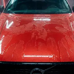 Czerwona maska samochodu z powłoką ceramiczną pokryta kroplami wody. Dowiedz się, jak myć auto z powłoką ceramiczną, by zachować jej blask.