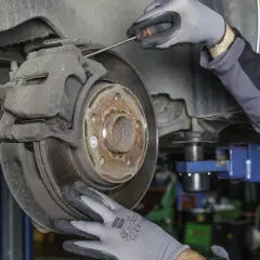 Mechanik w rękawiczkach sprawdza stan klocków hamulcowych przy tarczy hamulcowej samochodu.