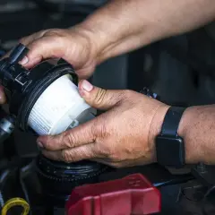 Ręce mechanika wymieniające filtr paliwa w samochodzie.