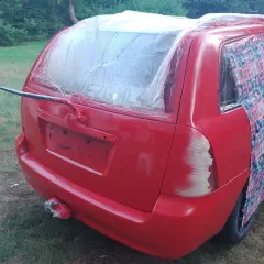 Czerwony samochód z zakrytą folią tylną szybą i częścią karoserii, przygotowywany do malowania.