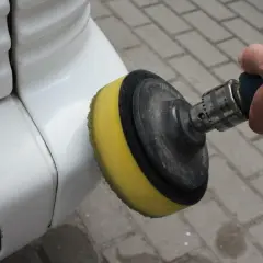 Ręka trzyma polerkę z żółtą gąbką, która jest używana do polerowania białego zderzaka. To pokazuje, jak polerować auto.