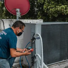 Technik w masce przeprowadza wymianę czujnika ciśnienia klimatyzacji, podłączając manometr do jednostki zewnętrznej.