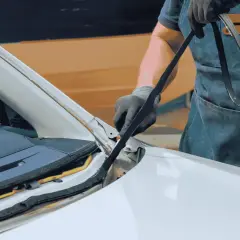 Rękawiczki i fartuch wskazują na precyzyjne klejenie szyb samochodowych. Mechanik przygotowuje się do montażu.