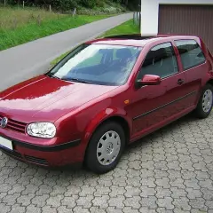 Czerwony Volkswagen Golf IV zaparkowany na podjeździe z kostki brukowej, obok garażu.