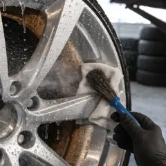 Czyszczenie felg aluminiowych: rękawiczka, pędzelek i środek do czyszczenia felg usuwają brud z mokrej felgi.