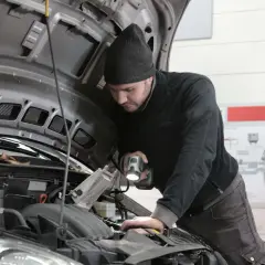Mechanik z latarką bada silnik, zastanawiając się, jak długo jeszcze wytrzyma stukający przegub.