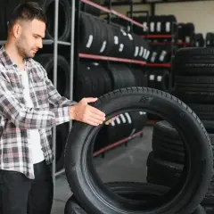 Mężczyzna w sklepie z oponami sprawdza nową oponę, zastanawiając się, czy nowe opony muszą się ułożyć.