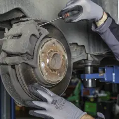 Mechanik w rękawiczkach sprawdza hamulce, by uniknąć bicia kierownicy przy hamowaniu.