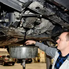 Mechanik spuszcza stary olej z samochodu. Pamiętaj o regularnej wymianie oleju w samochodzie co ile, by silnik działał sprawnie.