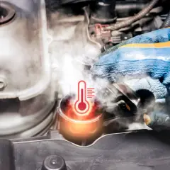 Rękawica mechanika sprawdza zbiorniczek wyrównawczy, z którego wydobywa się para. Widoczny symbol termometru wskazuje na **wysoką temperaturę płynu chłodniczego**.