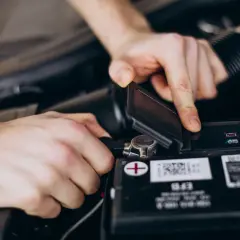 Dłonie mechanika podłączają klemę do akumulatora samochodowego.