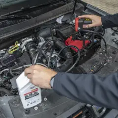 Mechanik próbuje zdiagnozować za wysoki poziom oleju w silniku diesla, podłączając urządzenie do akumulatora i trzymając butelkę oleju.