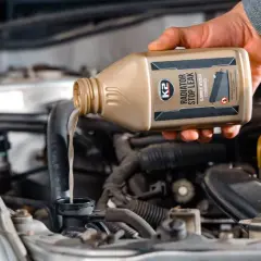 Dłoń wylewa płyn do chłodnicy z butelki K2 Radiator Stop Leak, wykonując wymianę płynu chłodniczego.