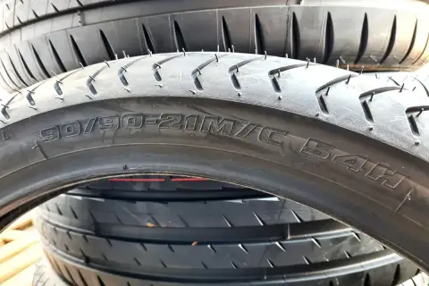 Czarne opony motocyklowe ułożone jedna na drugiej. Widoczny napis "90/90-21M/C 54H" wyjaśnia, co to jest profil opony.