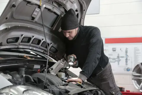 Mechanik z latarką bada silnik, zastanawiając się, jak długo jeszcze wytrzyma stukający przegub.