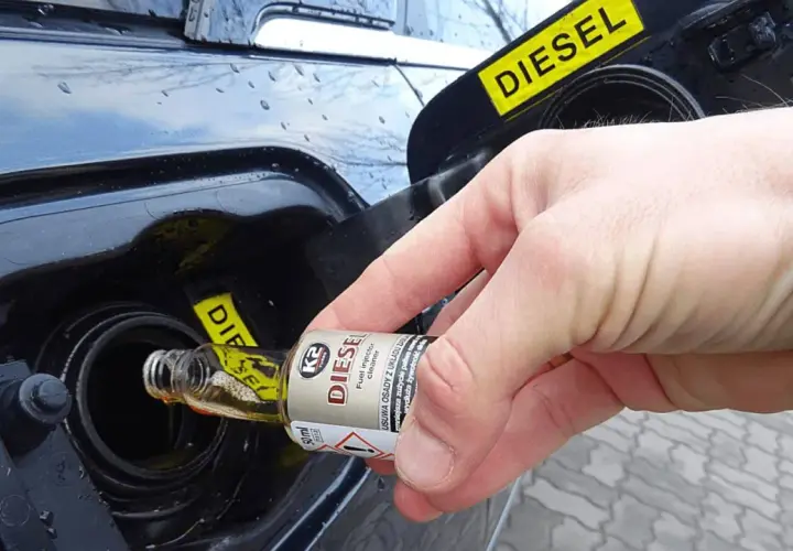 Dłoń wlewa dodatek do benzyny z małej buteleczki do baku diesla.