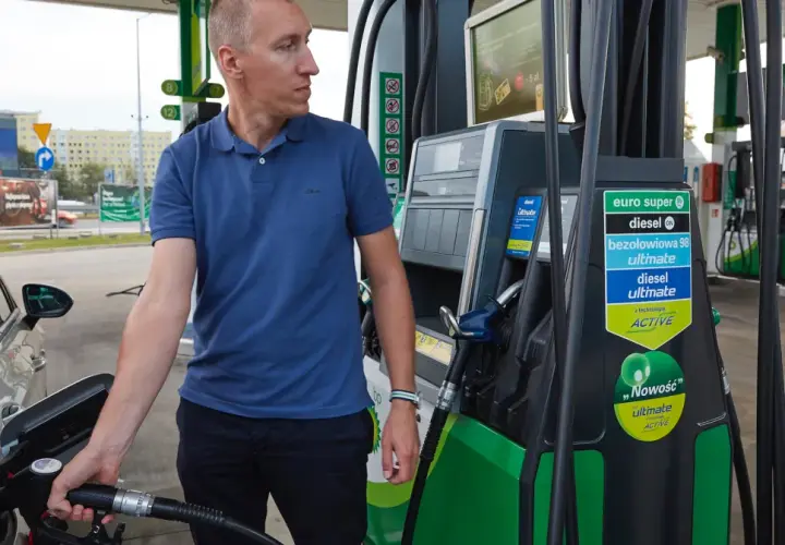 Mężczyzna tankuje samochód, pokazując, jak zatankować auto. Widoczna jest dystrybutor paliwa z różnymi rodzajami paliwa.