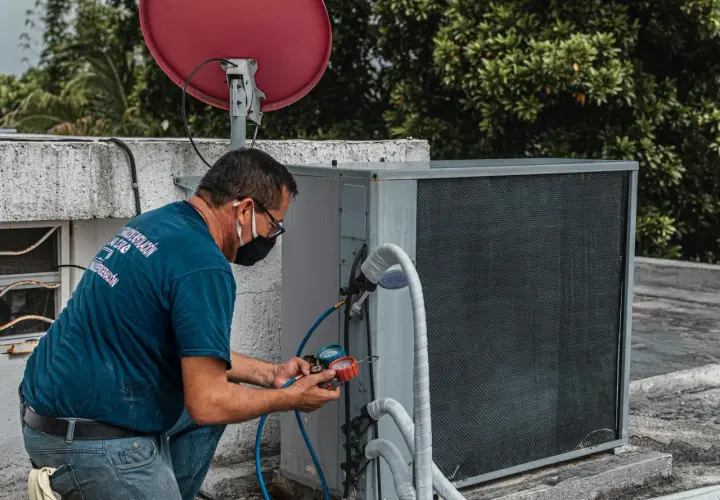 Technik w masce przeprowadza wymianę czujnika ciśnienia klimatyzacji, podłączając manometr do jednostki zewnętrznej.