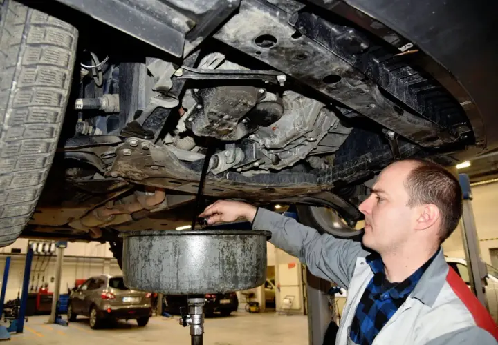 Mechanik spuszcza stary olej z samochodu. Pamiętaj o regularnej wymianie oleju w samochodzie co ile, by silnik działał sprawnie.