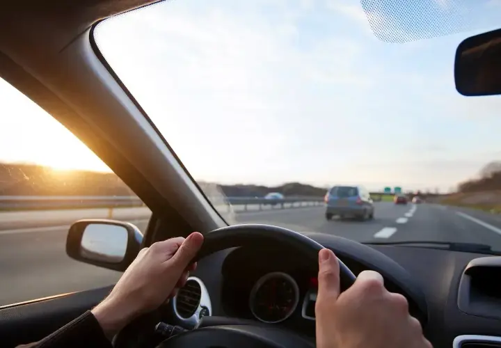 Widok z perspektywy kierowcy na autostradę z zachodzącym słońcem i innymi samochodami.