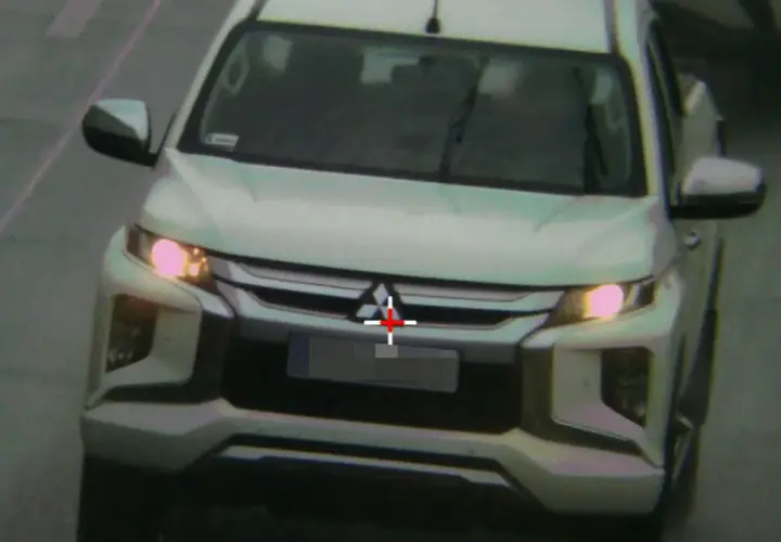 Biały pickup jedzie zderzakiem do przodu, z czerwonym krzyżem na grillu.
