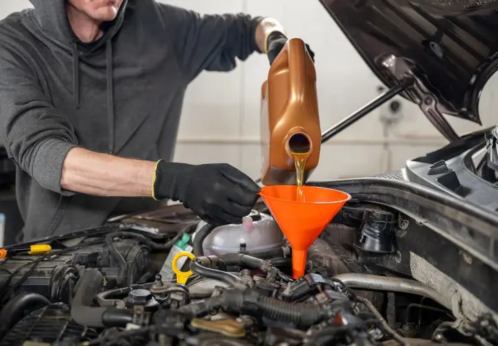 Mechanik w rękawiczkach nalewa olej silnikowy do silnika przez pomarańczowy lejek.
