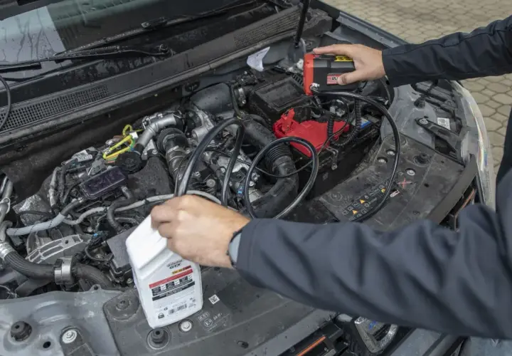 Mechanik próbuje zdiagnozować za wysoki poziom oleju w silniku diesla, podłączając urządzenie do akumulatora i trzymając butelkę oleju.