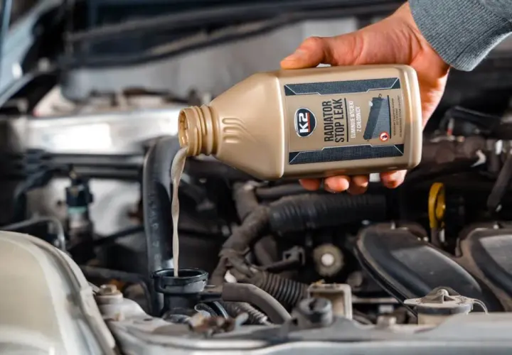 Dłoń wylewa płyn do chłodnicy z butelki K2 Radiator Stop Leak, wykonując wymianę płynu chłodniczego.