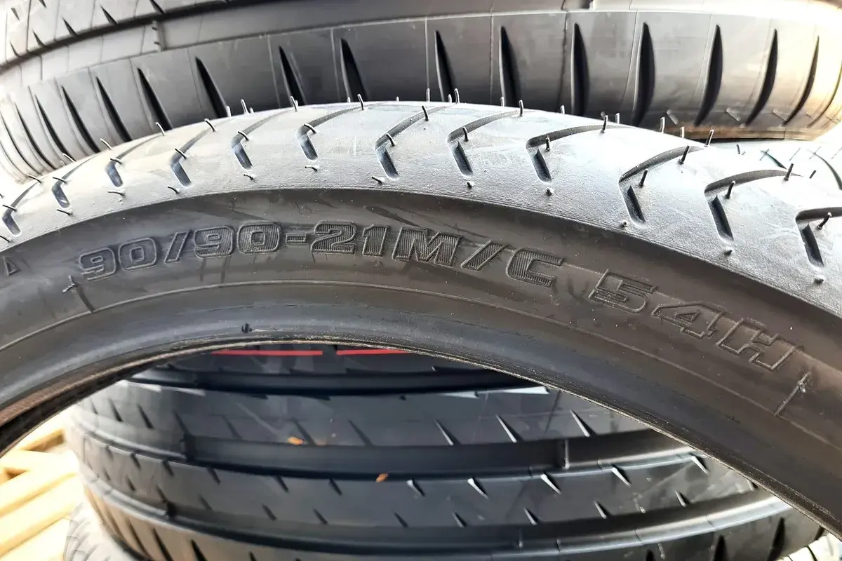 Czarne opony motocyklowe ułożone jedna na drugiej. Widoczny napis "90/90-21M/C 54H" wyjaśnia, co to jest profil opony.