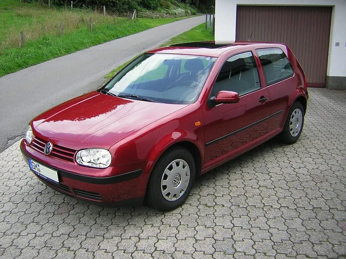 Czerwony Volkswagen Golf IV zaparkowany na podjeździe z kostki brukowej, obok garażu.