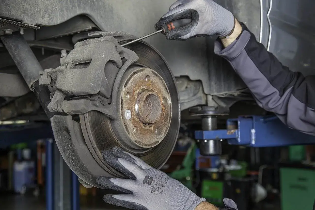 Mechanik w rękawiczkach sprawdza hamulce, by uniknąć bicia kierownicy przy hamowaniu.