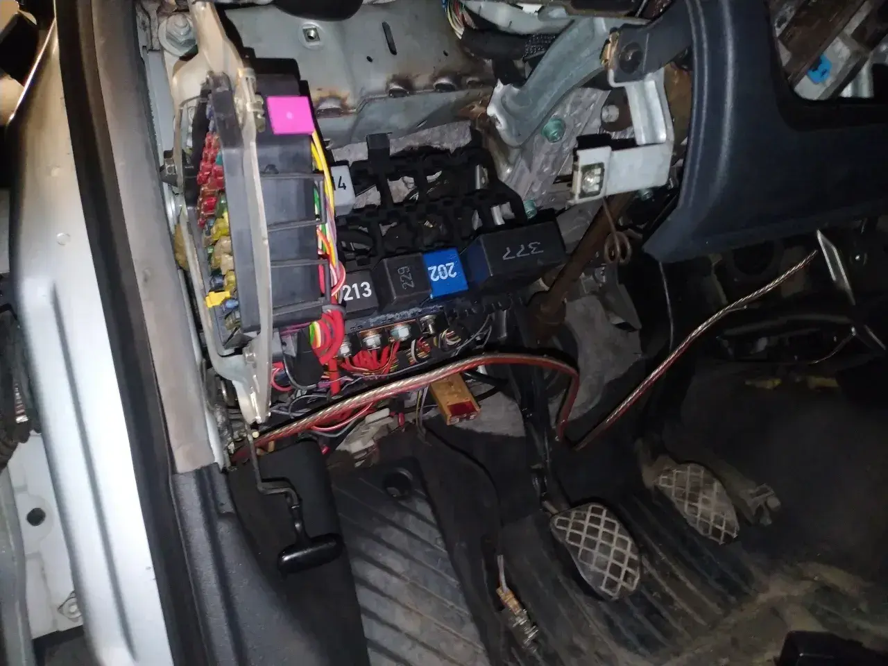 Widok na skrzynkę z bezpiecznikami i przekaźnikami w Audi A4 B6. Widać kolorowe bezpieczniki i kable.