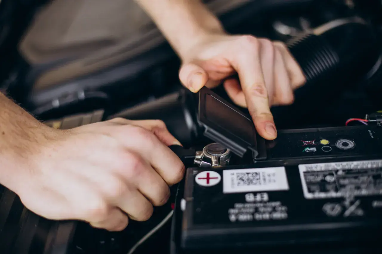Dłonie mechanika podłączają klemę do akumulatora samochodowego.