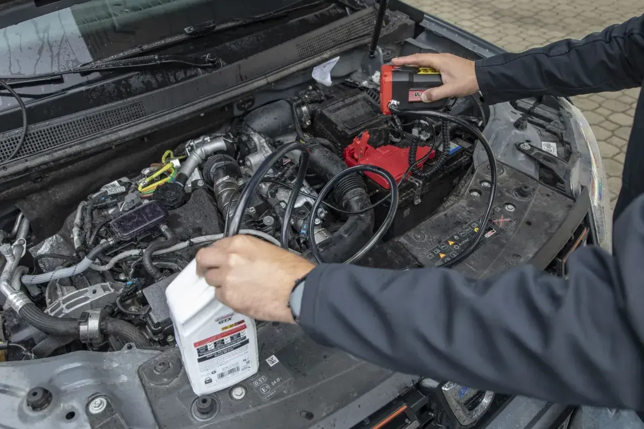 Mechanik próbuje zdiagnozować za wysoki poziom oleju w silniku diesla, podłączając urządzenie do akumulatora i trzymając butelkę oleju.