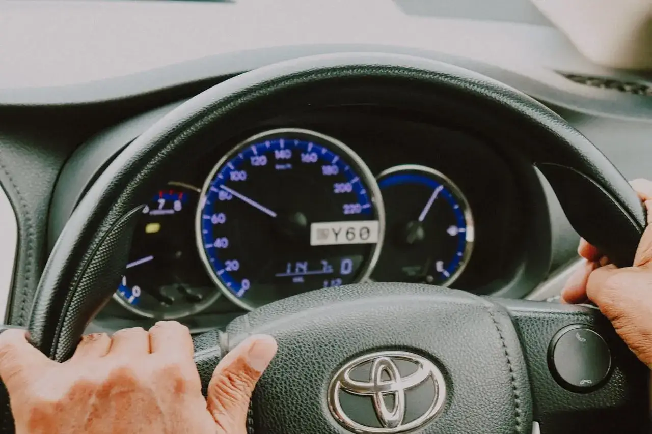 Ręce na kierownicy Toyoty, kontrolki na desce rozdzielczej sugerują elektryczne wspomaganie kierownicy usterki.
