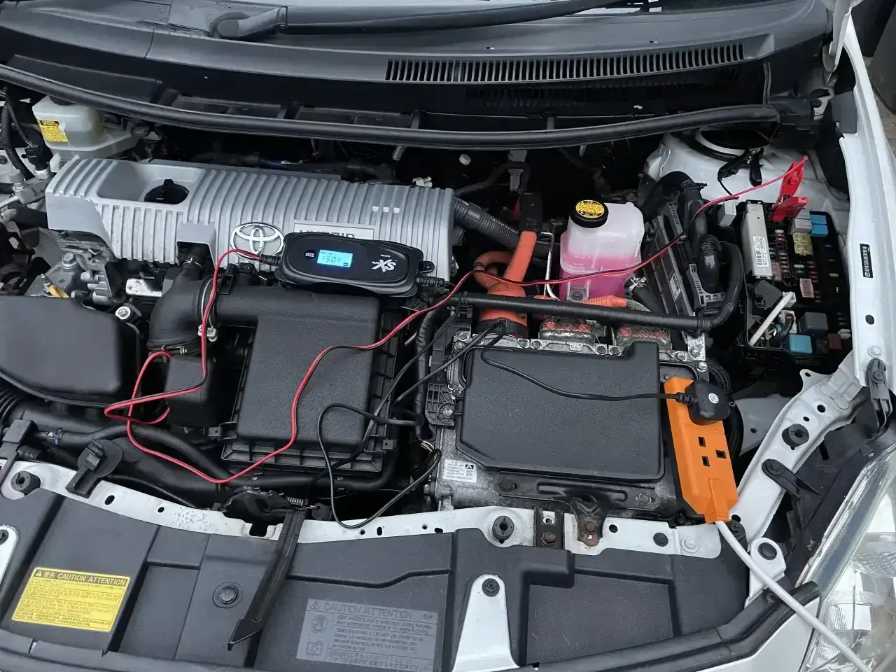 Silnik Toyota Yaris Hybrid. Akumulator 12V znajduje się pod czarną pokrywą z przodu, po prawej stronie. Podłączono do niego prostownik.