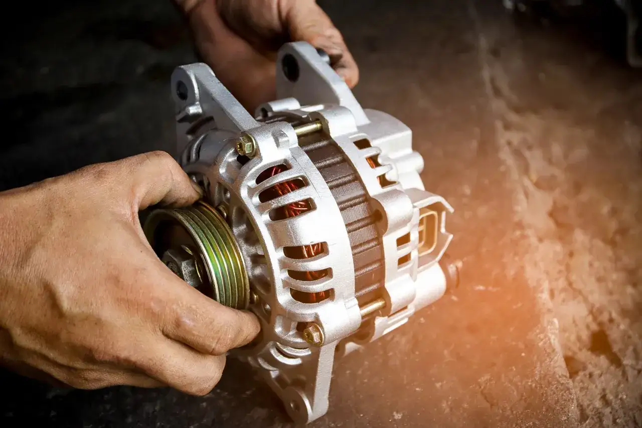 Dłonie mechanika trzymają alternator do auta, gotowy do montażu.