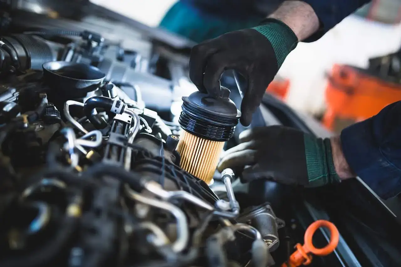 Mechanik w rękawiczkach wymienia filtr oleju w silniku samochodu. To prosty sposób, jak wymienić filtr i zadbać o auto.
